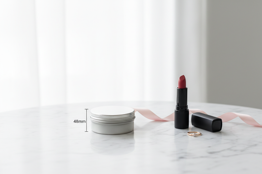 Caja metálica mini redonda 48x28 mm plateada cerrada sobre mármol blanco con lápiz labial y anillo para referencia de tamaño